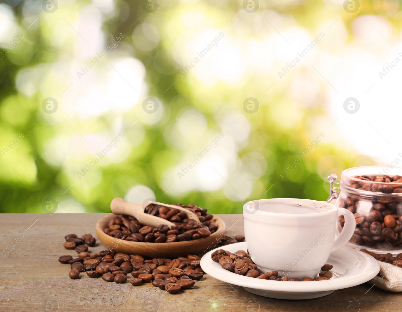 Image of Cup of aromatic hot coffee and beans on wooden table outdoors 