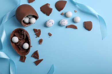 Photo of Tasty broken chocolate eggs with different sweets on light blue background, flat lay. Space for text
