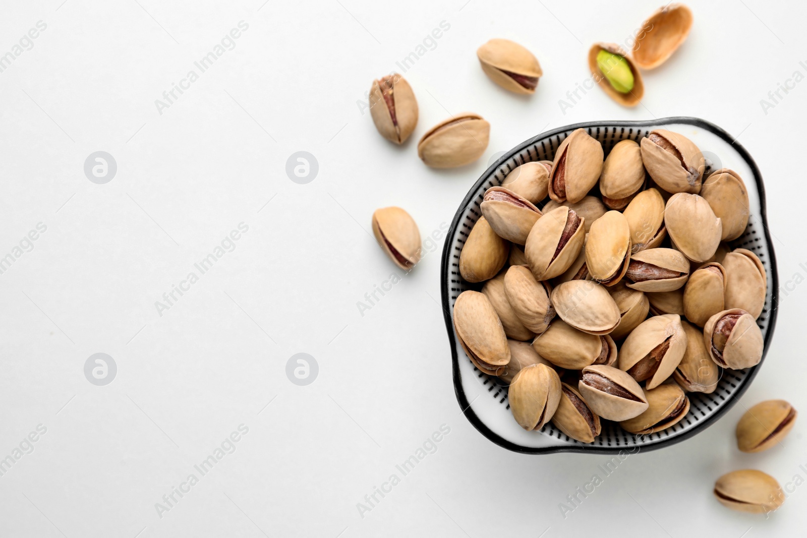 Photo of Bowl and pistachio nuts on white background, flat lay. Space for text