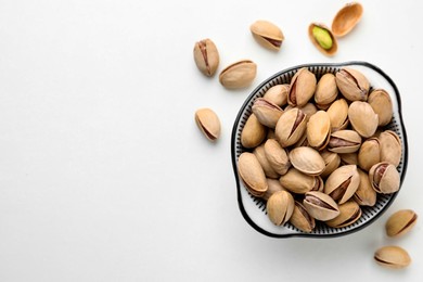 Photo of Bowl and pistachio nuts on white background, flat lay. Space for text