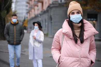 Photo of Young woman in medical face mask walking outdoors. Personal protection during COVID-19 pandemic