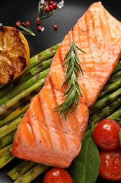 Photo of Tasty grilled salmon with tomatoes, asparagus and spices on plate, top view