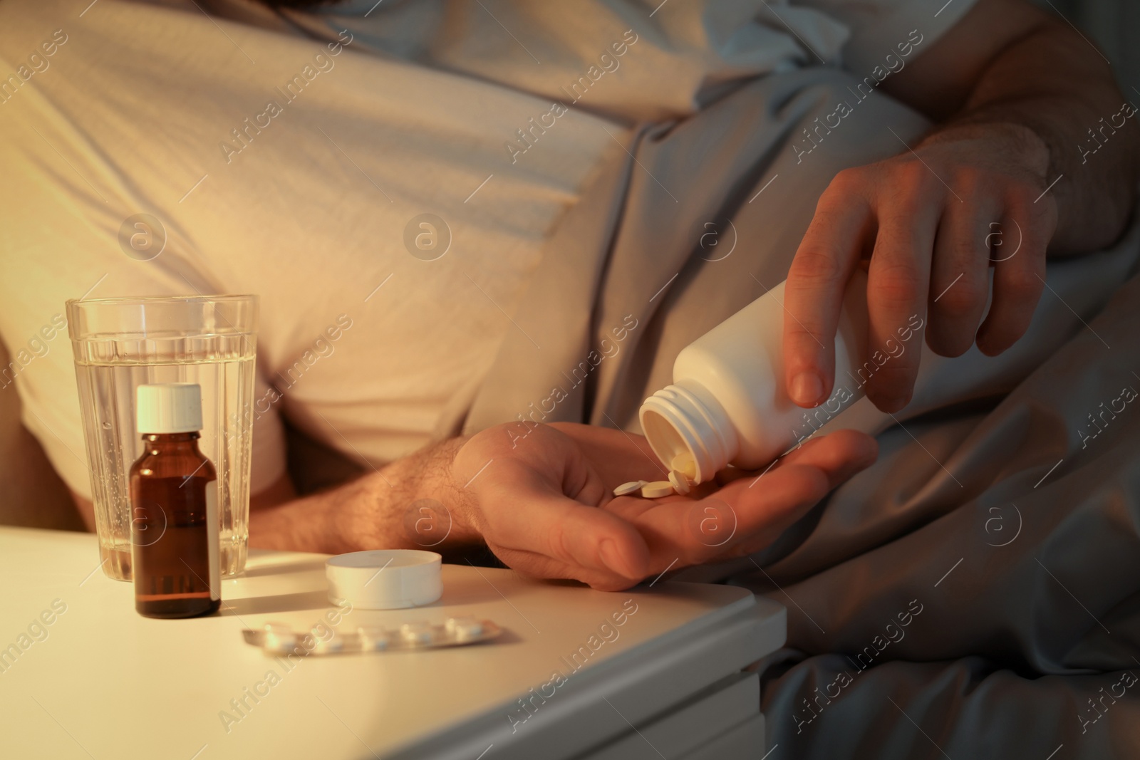 Photo of Man with bottle of pills in bed at night, closeup. Insomnia concept