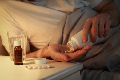 Photo of Man with bottle of pills in bed at night, closeup. Insomnia concept