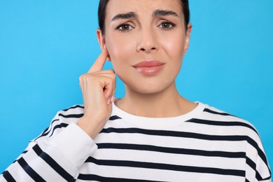 Photo of Young woman suffering from ear pain on light blue background, closeup