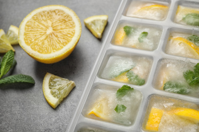 Ice cubes with lemon and mint in tray on grey table, closeup