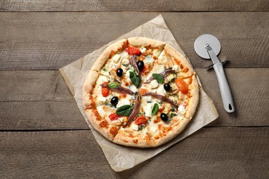 Photo of Tasty pizza with anchovies and cutter on wooden table, top view
