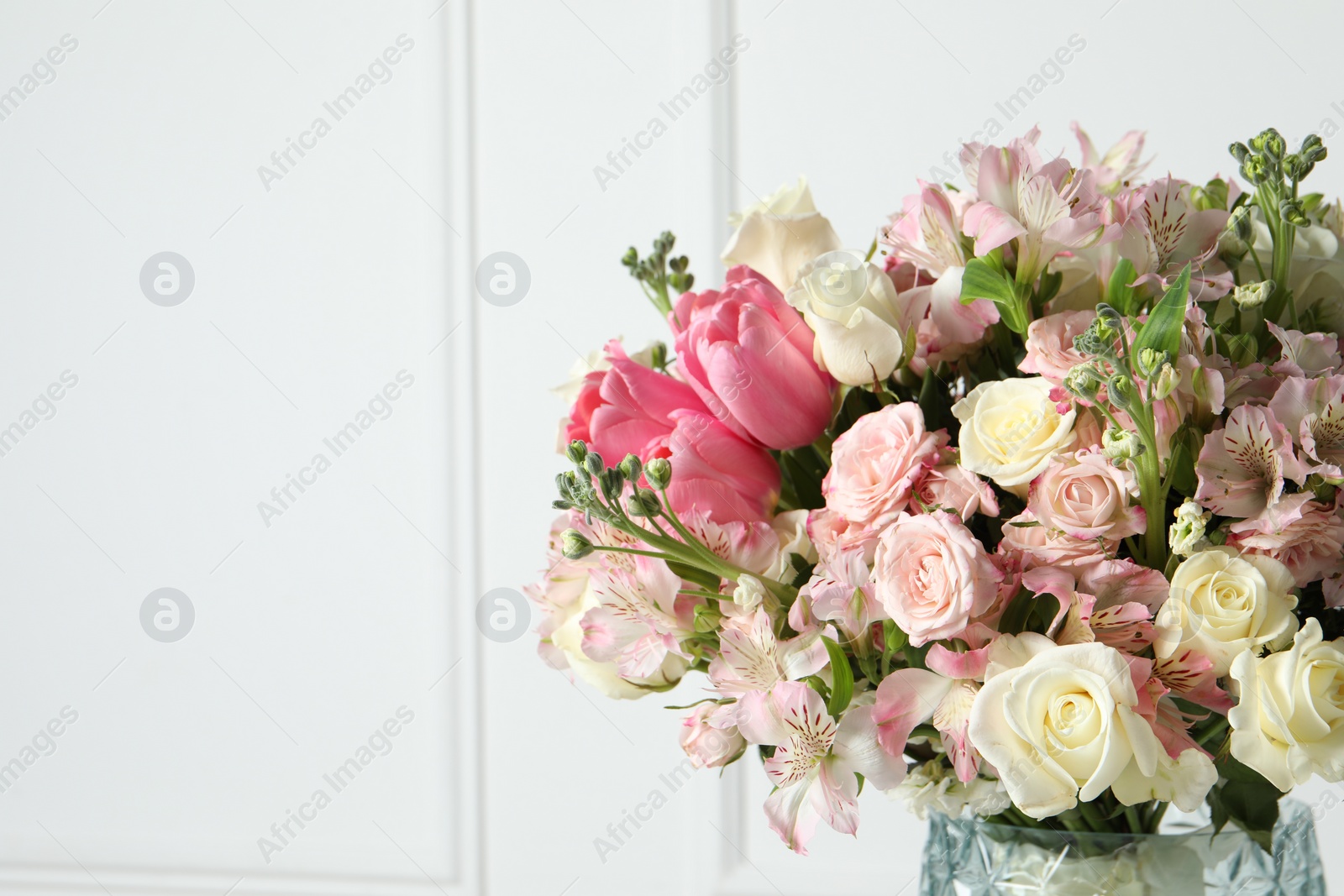 Photo of Beautiful bouquet of fresh flowers in vase near white wall. Space for text