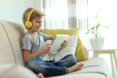 Cute little boy with headphones and tablet listening to audiobook at home