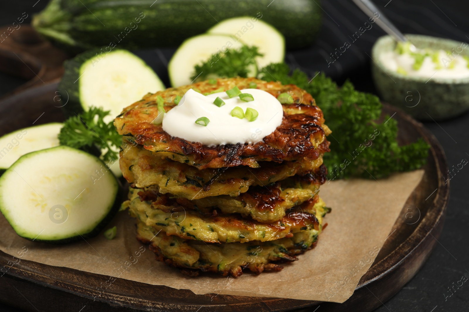 Photo of Delicious zucchini fritters with sour cream served on black table, closeup