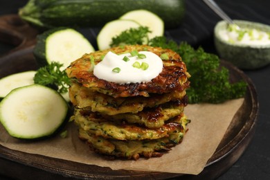 Photo of Delicious zucchini fritters with sour cream served on black table, closeup