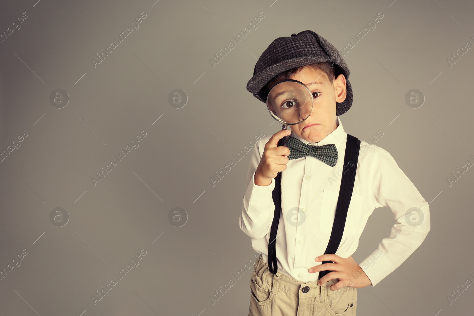 Photo of Little boy with magnifying glass playing detective on grey background. Space for text