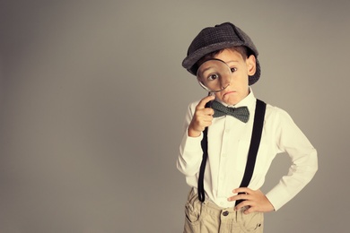 Photo of Little boy with magnifying glass playing detective on grey background. Space for text