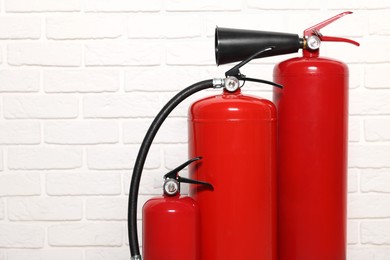 Photo of Red fire extinguishers near white brick wall, space for text