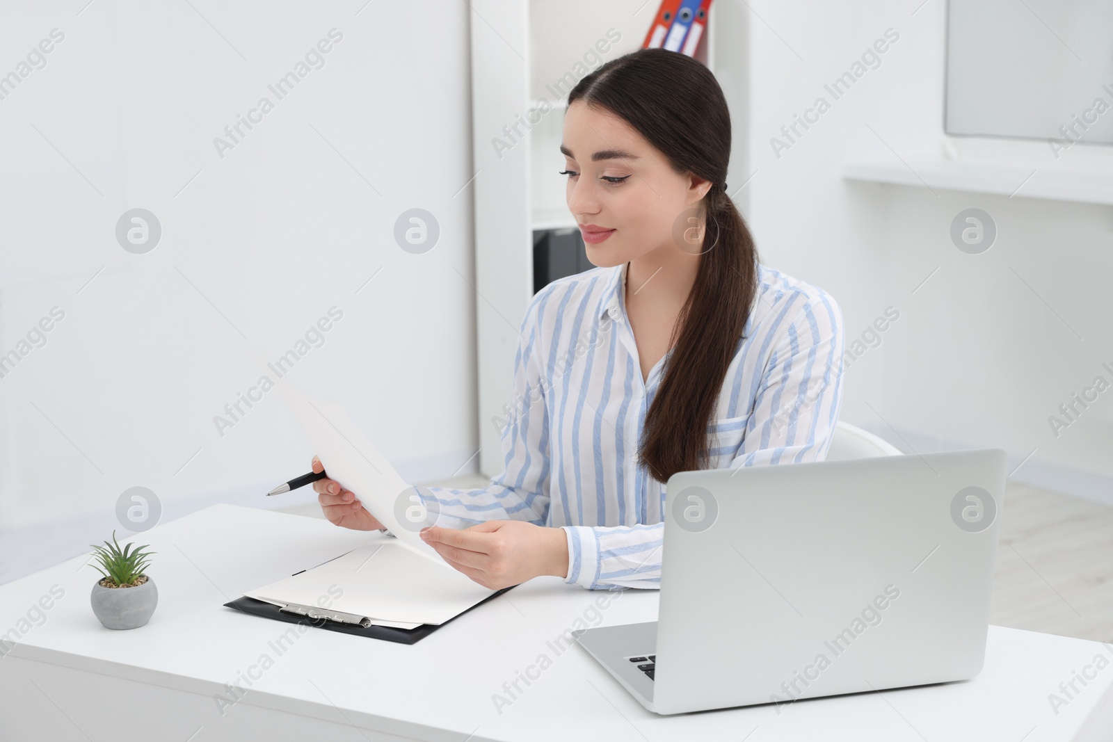 Photo of Young female intern working with laptop at table in office