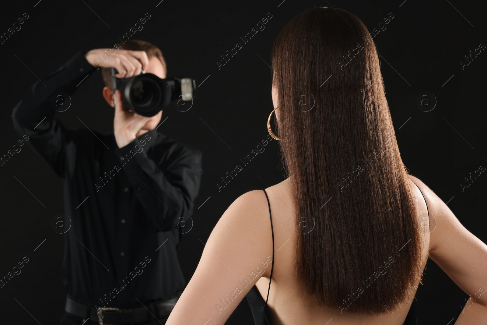 Photo of Professional photographer taking picture of model on black background, selective focus