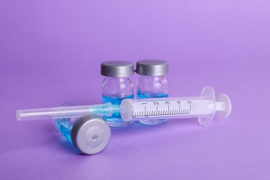 Photo of Disposable syringe with needle and vials on violet background