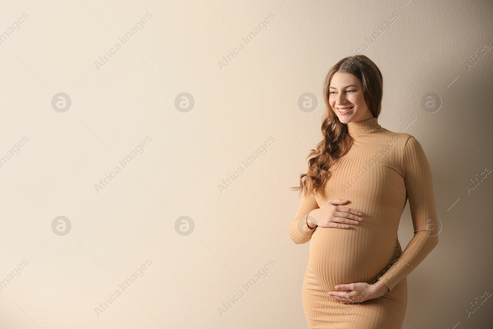 Photo of Happy pregnant woman touching her belly on beige background. Space for text