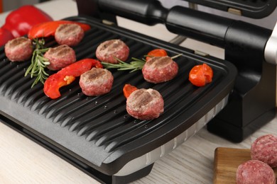 Photo of Electric grill with vegetables, meat balls and rosemary on table, closeup