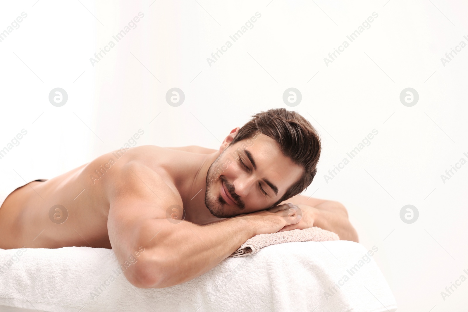 Photo of Handsome young man relaxing on massage table against light background, space for text. Spa salon