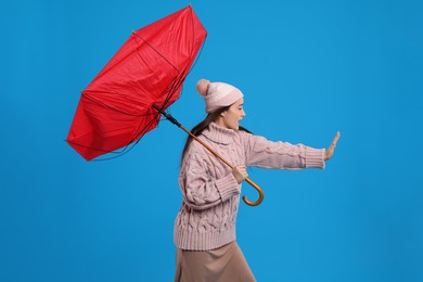 Photo of Young woman with umbrella caught in gust of wind on light blue background