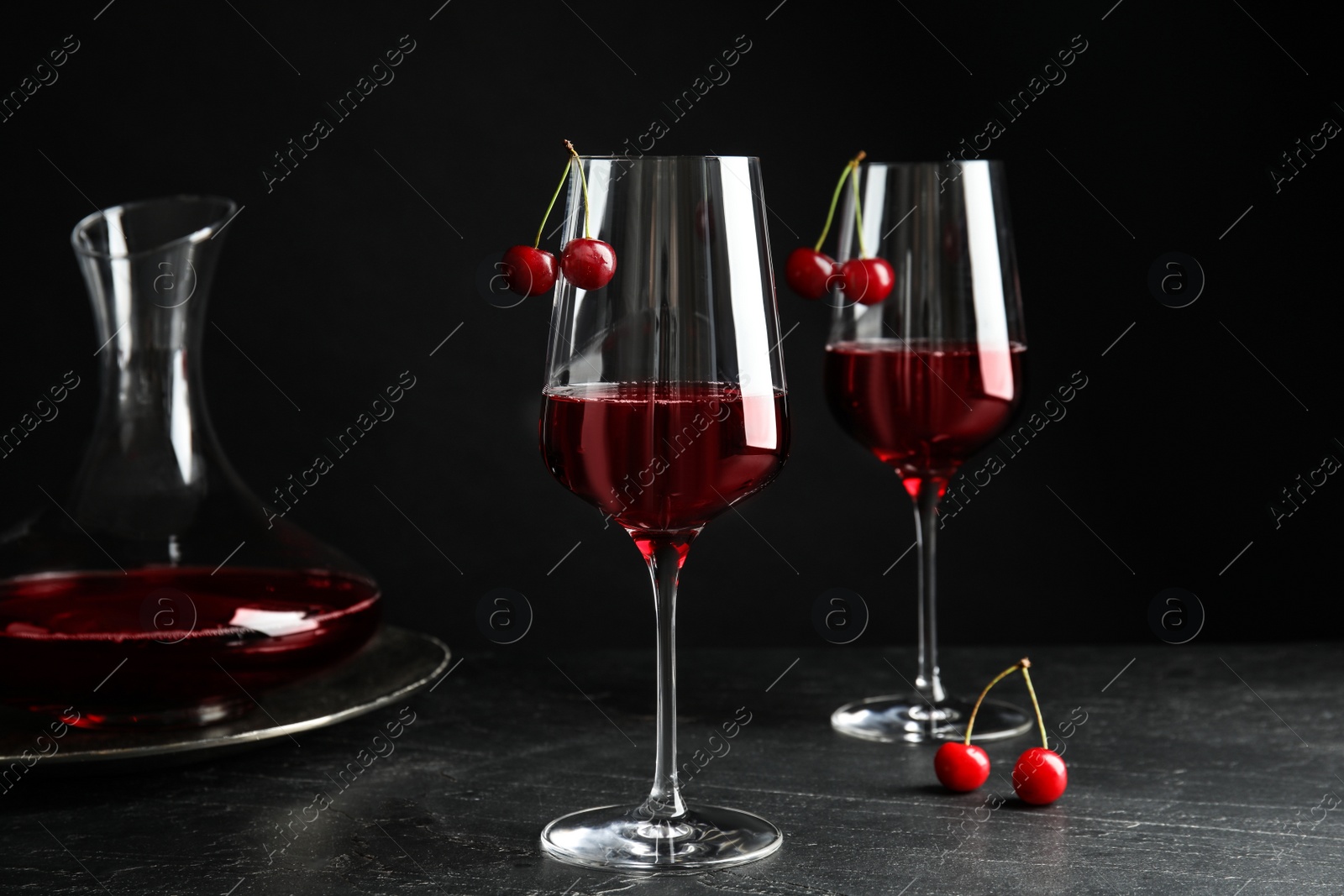 Photo of Delicious cherry wine with ripe juicy berries on grey table against black background