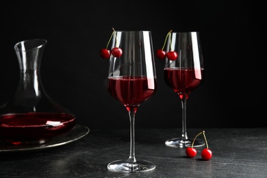 Photo of Delicious cherry wine with ripe juicy berries on grey table against black background