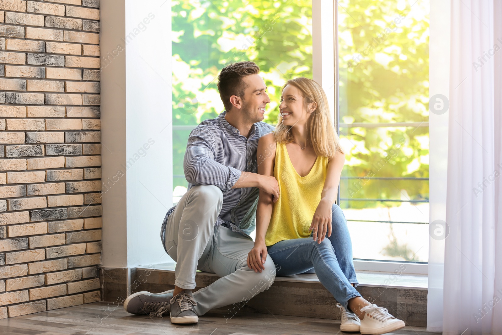 Photo of Happy young couple sitting near window at home