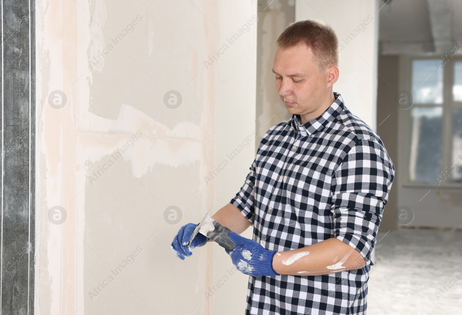 Photo of Worker with putty knives and plaster near wall indoors. Home renovation