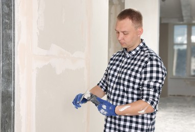Photo of Worker with putty knives and plaster near wall indoors. Home renovation