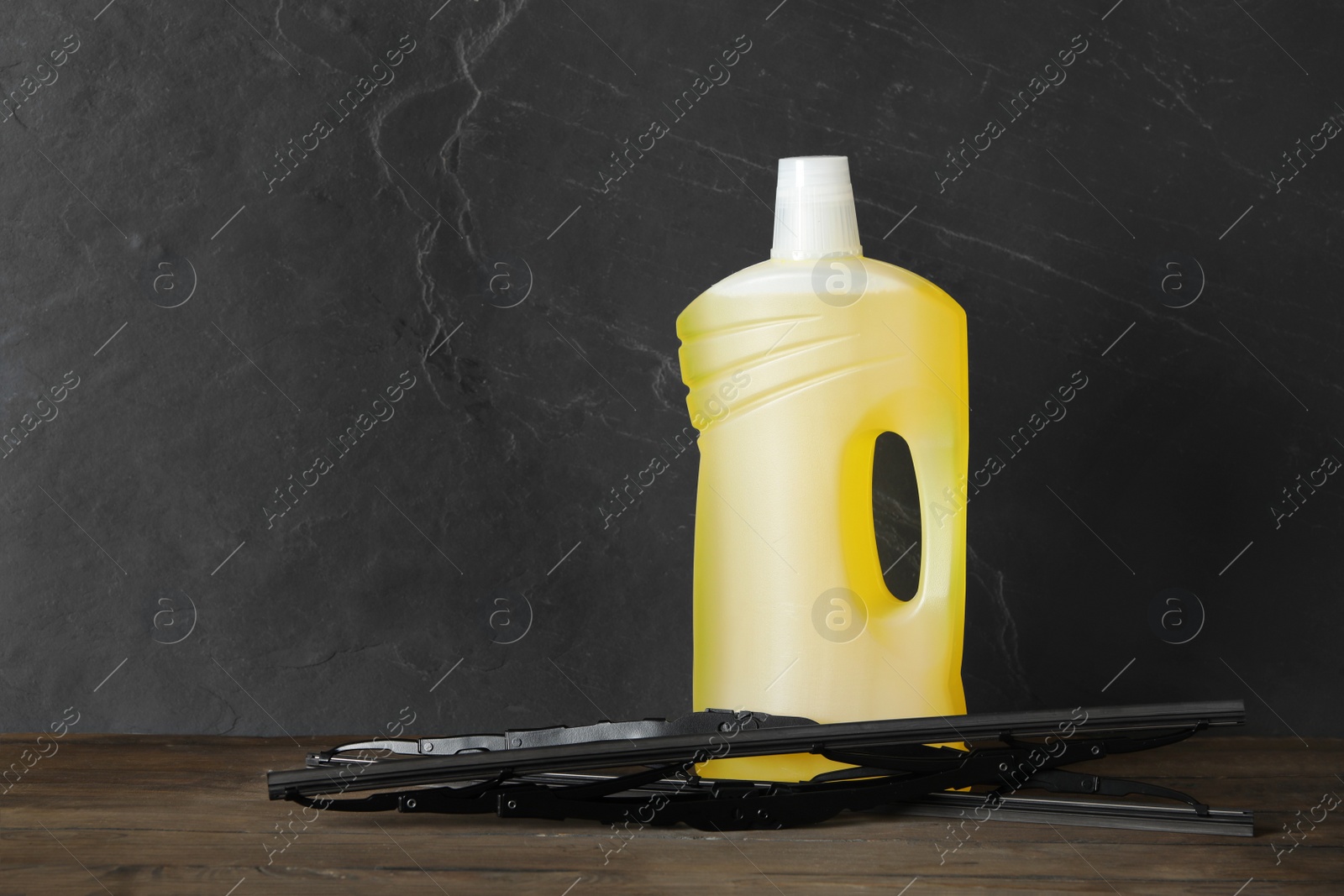 Photo of Bottle of windshield washer fluid and wipers on wooden table against black background. Space for text