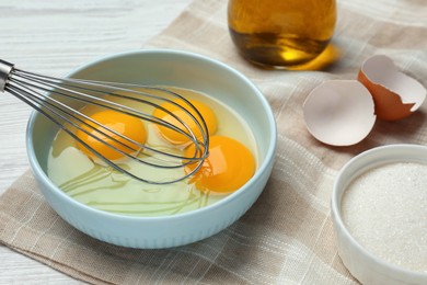 Photo of Whisking eggs in bowl on white wooden table, closeup