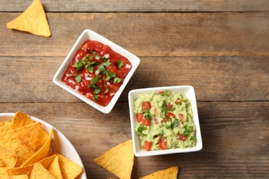 Photo of Bowl of delicious mexican nachos chips and sauces on wooden table, flat lay