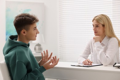 Psychologist working with teenage boy at table in office