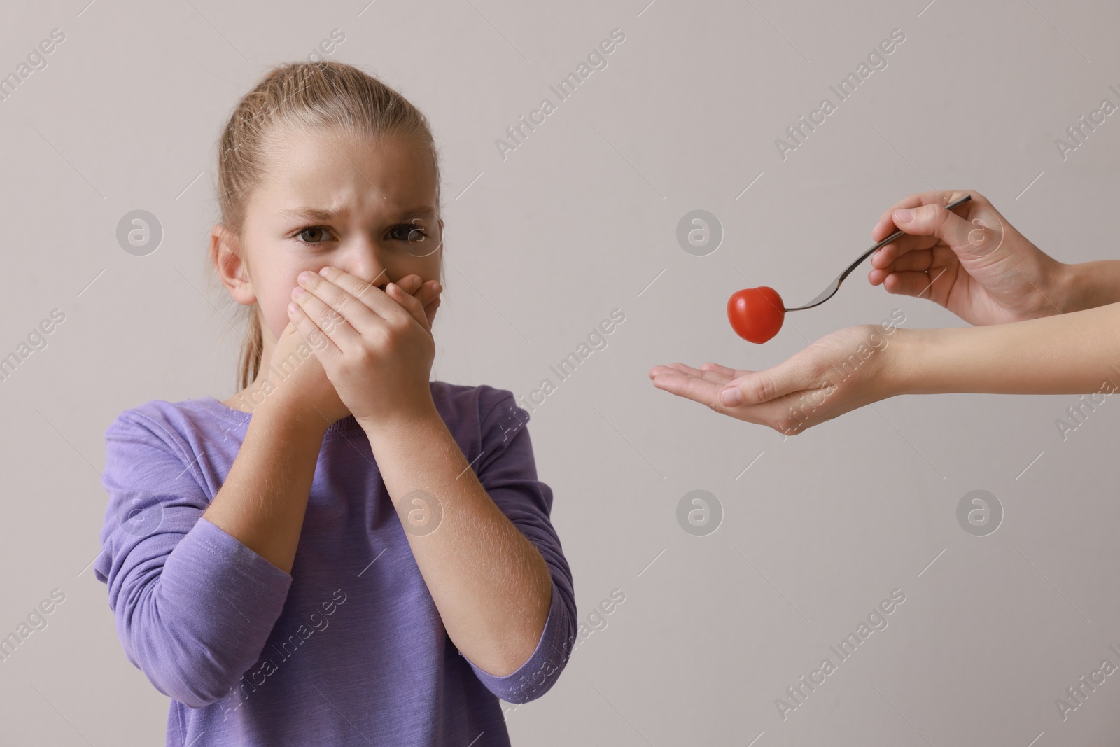 Photo of Cute little girl covering mouth and refusing to eat tomato on grey background