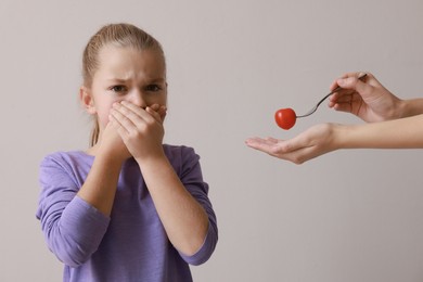 Photo of Cute little girl covering mouth and refusing to eat tomato on grey background