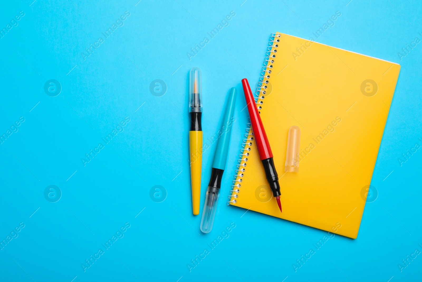 Photo of Yellow notebook and markers on light blue background, flat lay. Space for text