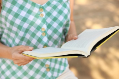 Young woman reading book outdoors, closeup view