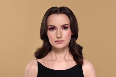 Portrait of beautiful young woman with makeup and gorgeous hair styling on beige background