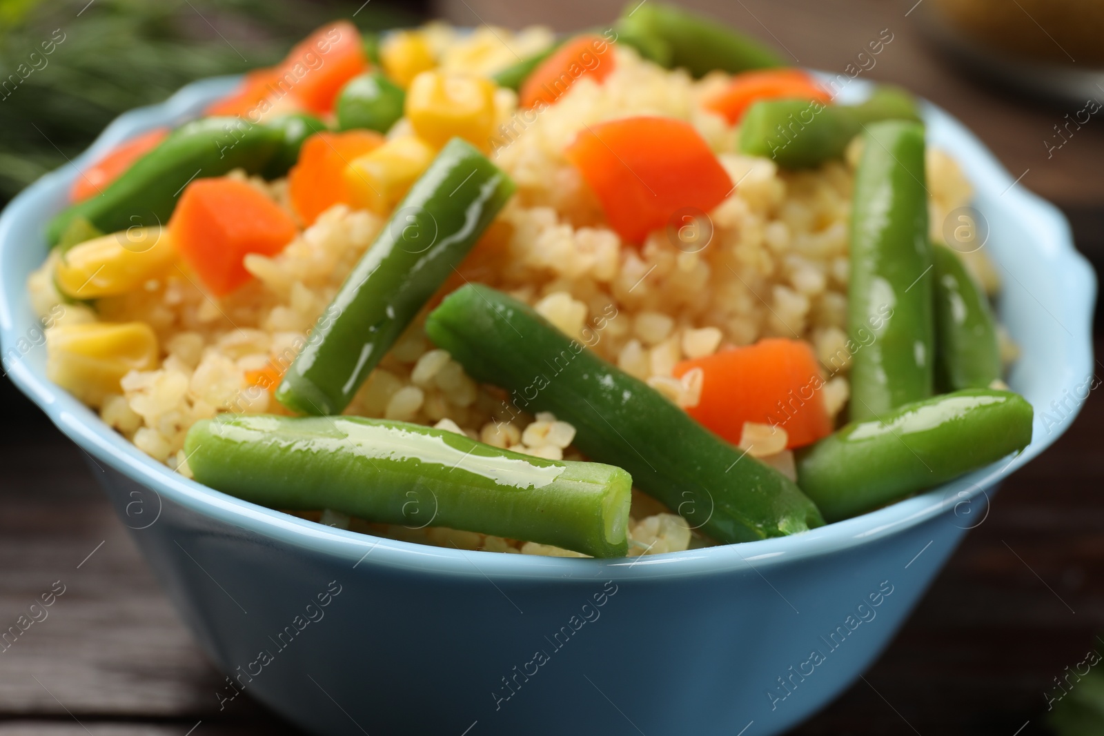 Photo of Delicious bulgur with vegetables in bowl on table, closeup