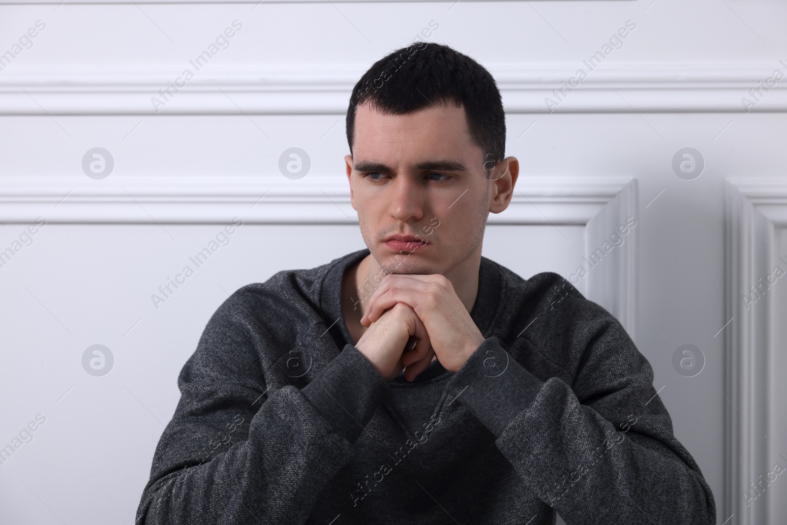 Photo of Sad man sitting near white wall indoors