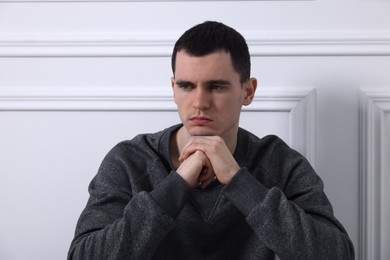 Photo of Sad man sitting near white wall indoors