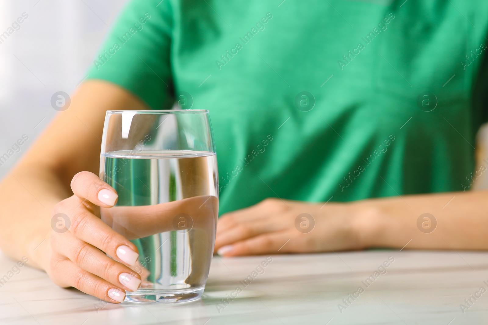 Photo of Healthy habit. Woman with glass of fresh water at white table, closeup
