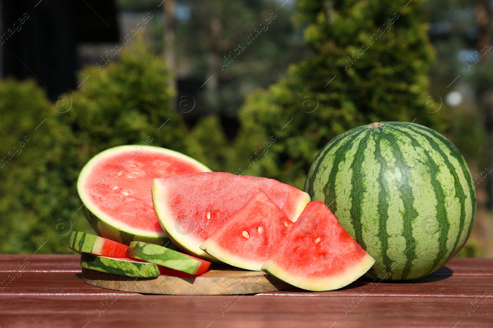 Photo of Delicious cut and whole ripe watermelons on wooden table outdoors