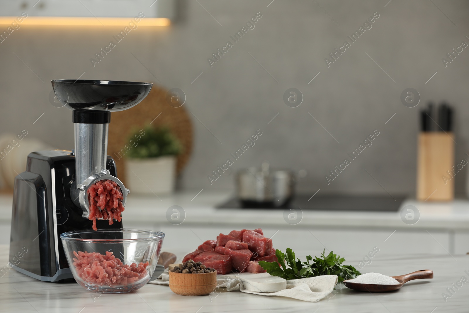Photo of Electric meat grinder with beef mince, parsley, salt and peppercorns on white table in kitchen
