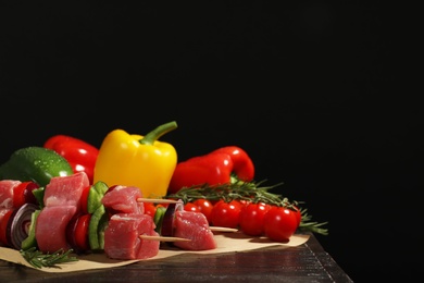 Photo of Skewers with fresh raw meat and vegetables on table against dark background. Space for text