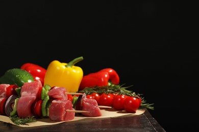 Skewers with fresh raw meat and vegetables on table against dark background. Space for text