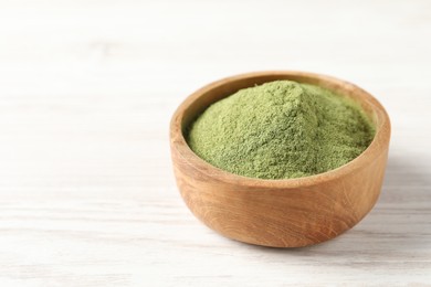 Photo of Wheat grass powder in bowl on white wooden table, closeup. Space for text