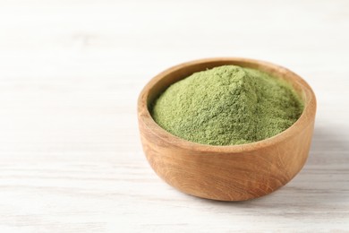 Wheat grass powder in bowl on white wooden table, closeup. Space for text