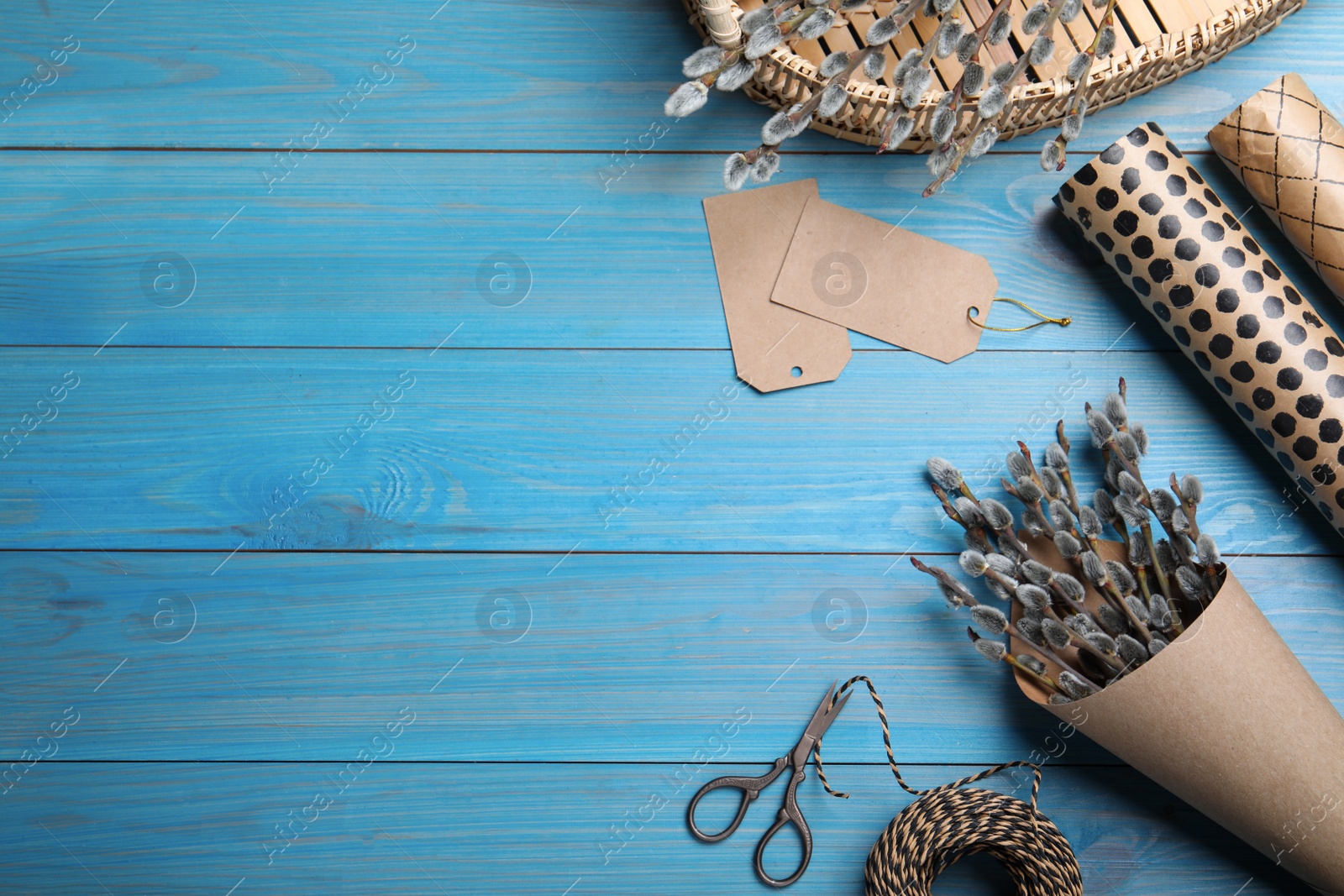 Photo of Beautiful bouquet of pussy willow branches and wrapping materials on light blue wooden table, flat lay. Space for text